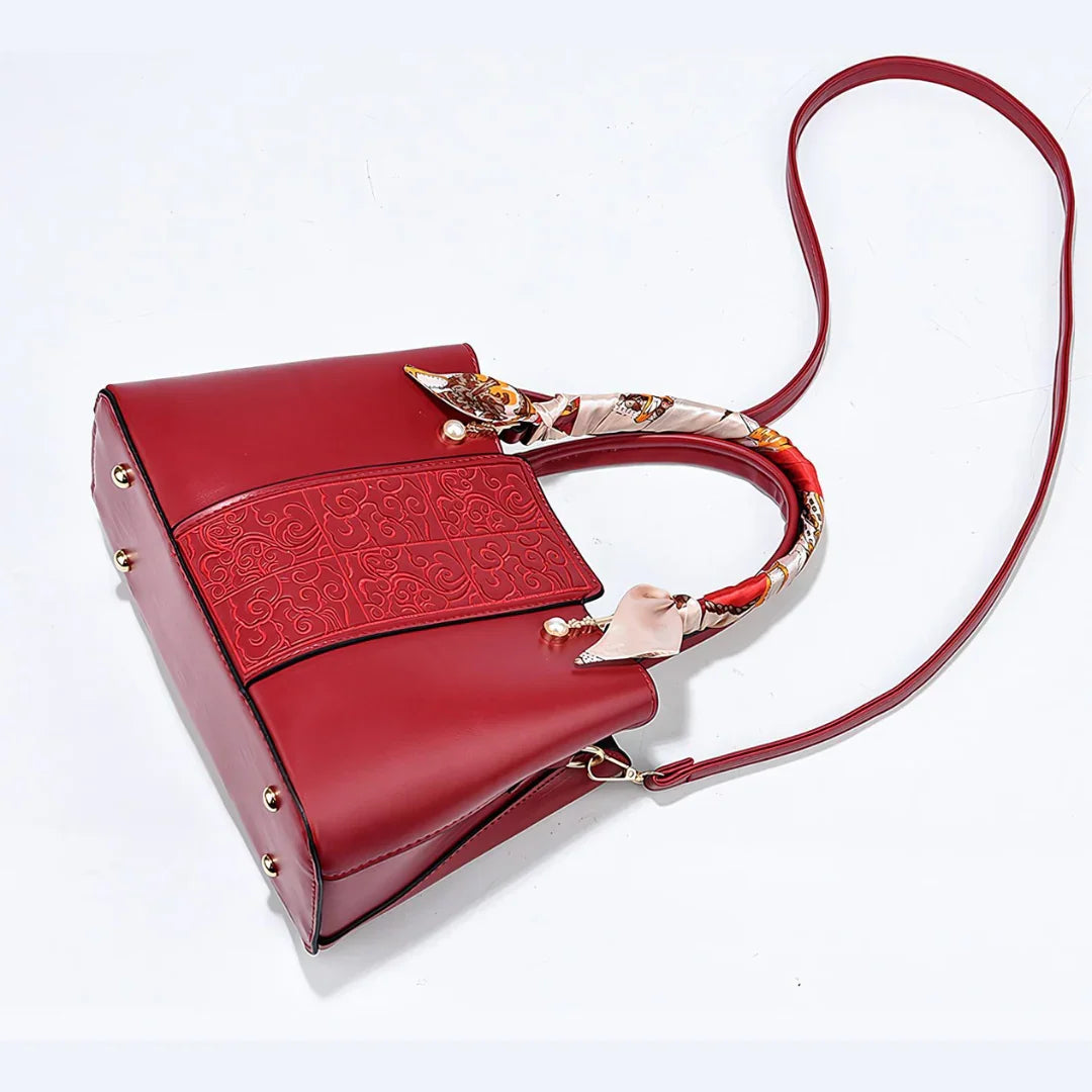 Red leather handbag with embossed pattern, printed scarf handle, long strap on white background
