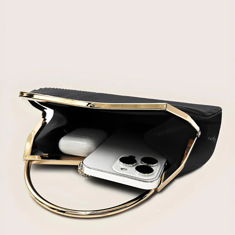 Black clutch purse with gold handle, open to show smartphone and earbuds inside