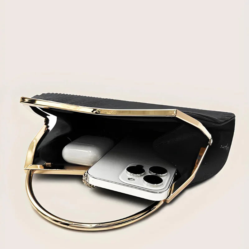 Black clutch purse with gold handle, open to show smartphone and earbuds inside