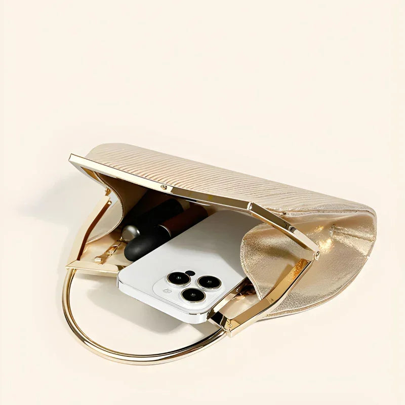 Gold metallic clutch bag with phone and lipstick on cream background