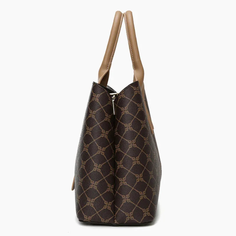 Side view of brown patterned tote bag with beige leather handles on white background