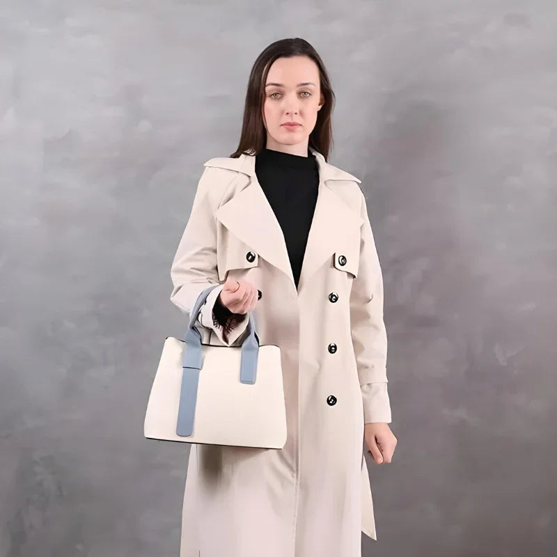 Woman in beige trench coat holding a stylish white handbag with blue handles