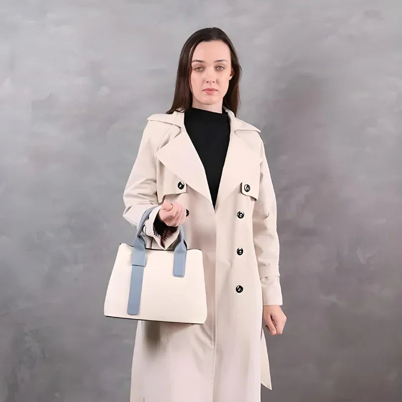 Woman in beige trench coat holding a stylish white handbag with blue handles