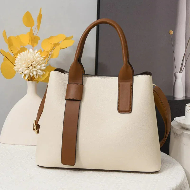 Beige tote bag with brown leather handles on white table, minimalist decor background