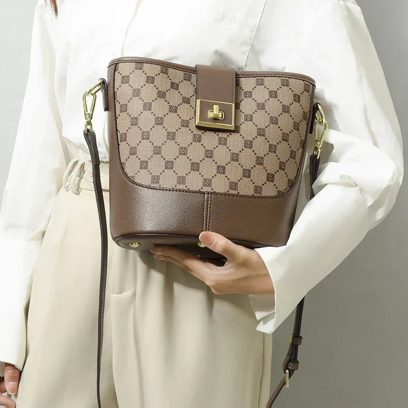 Woman holding brown designer crossbody bucket bag with gold hardware and geometric pattern