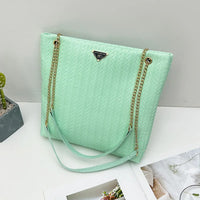 Mint green woven tote bag with gold chain straps on white table