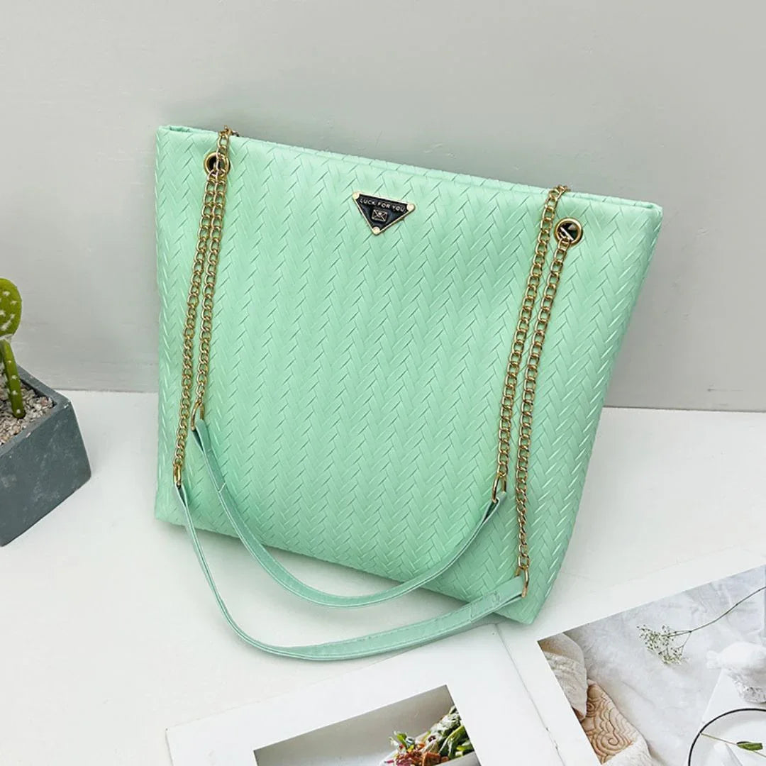 Mint green woven tote bag with gold chain straps on white table