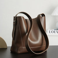 Minimalist brown leather shoulder bag on a modern desk with books and lamp