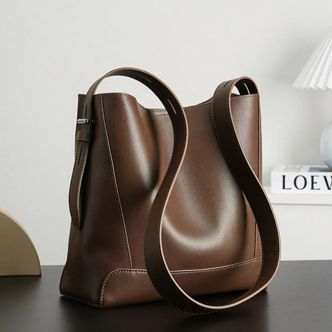 Minimalist brown leather shoulder bag on a modern desk with books and lamp
