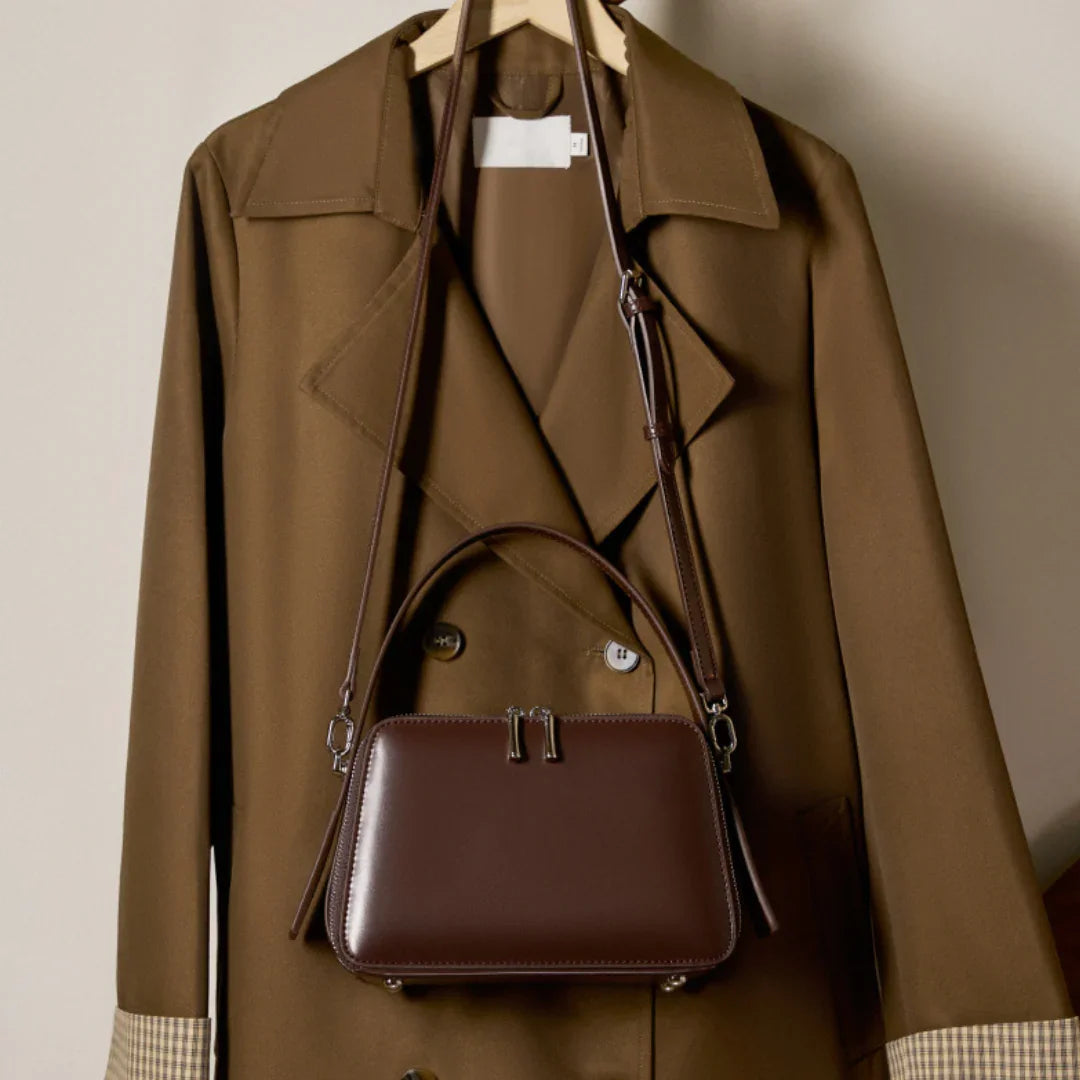 Brown leather handbag on tan trench coat with plaid cuffs, hanging on a wooden hanger