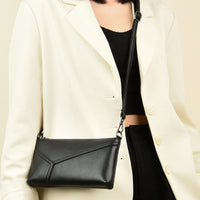 Woman in white blazer carries a black leather crossbody bag with geometric stitching