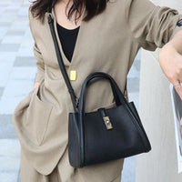 Woman in beige suit carrying black leather structured handbag with gold clasp