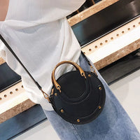 Round black crossbody handbag with gold studs, worn with white blouse and blue jeans