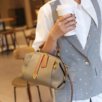 Woman in checkered vest holding taupe leather handbag and coffee cup in cafe