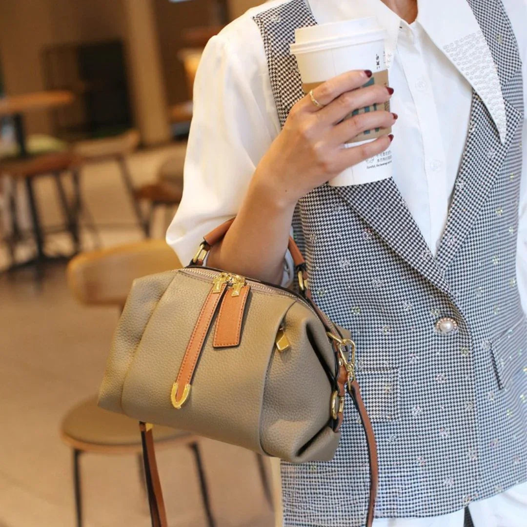 Woman in checkered vest holding taupe leather handbag and coffee cup in cafe