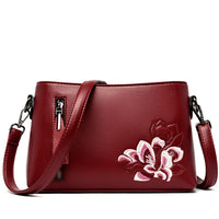 Red leather crossbody bag with pink floral embroidery and front zipper pocket