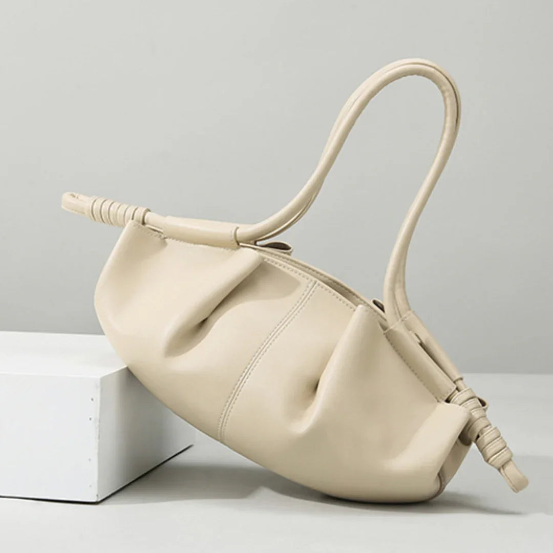Beige leather handbag with ruched design and curved handle on minimalist background