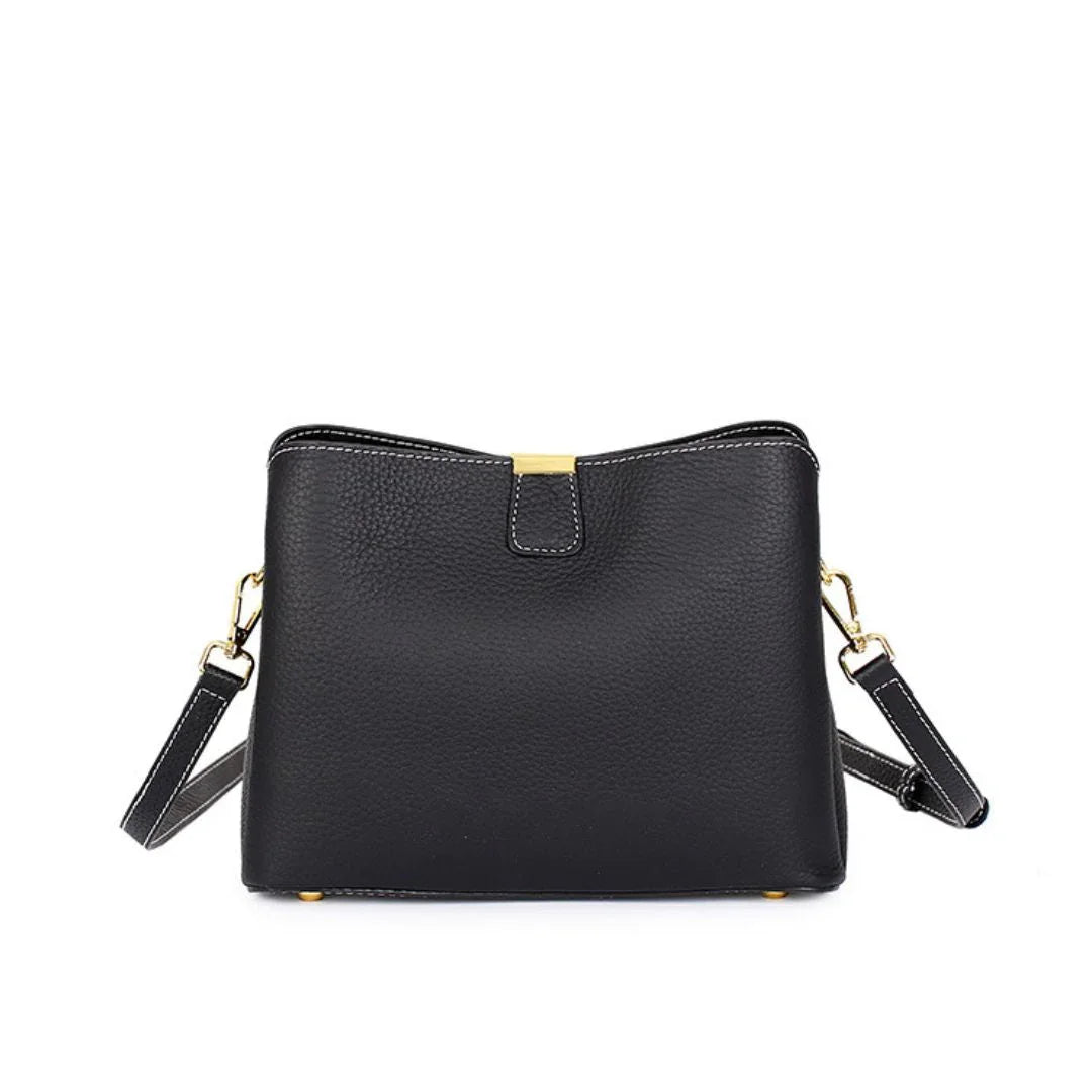 Black leather crossbody bag with gold hardware and white stitching on a white background