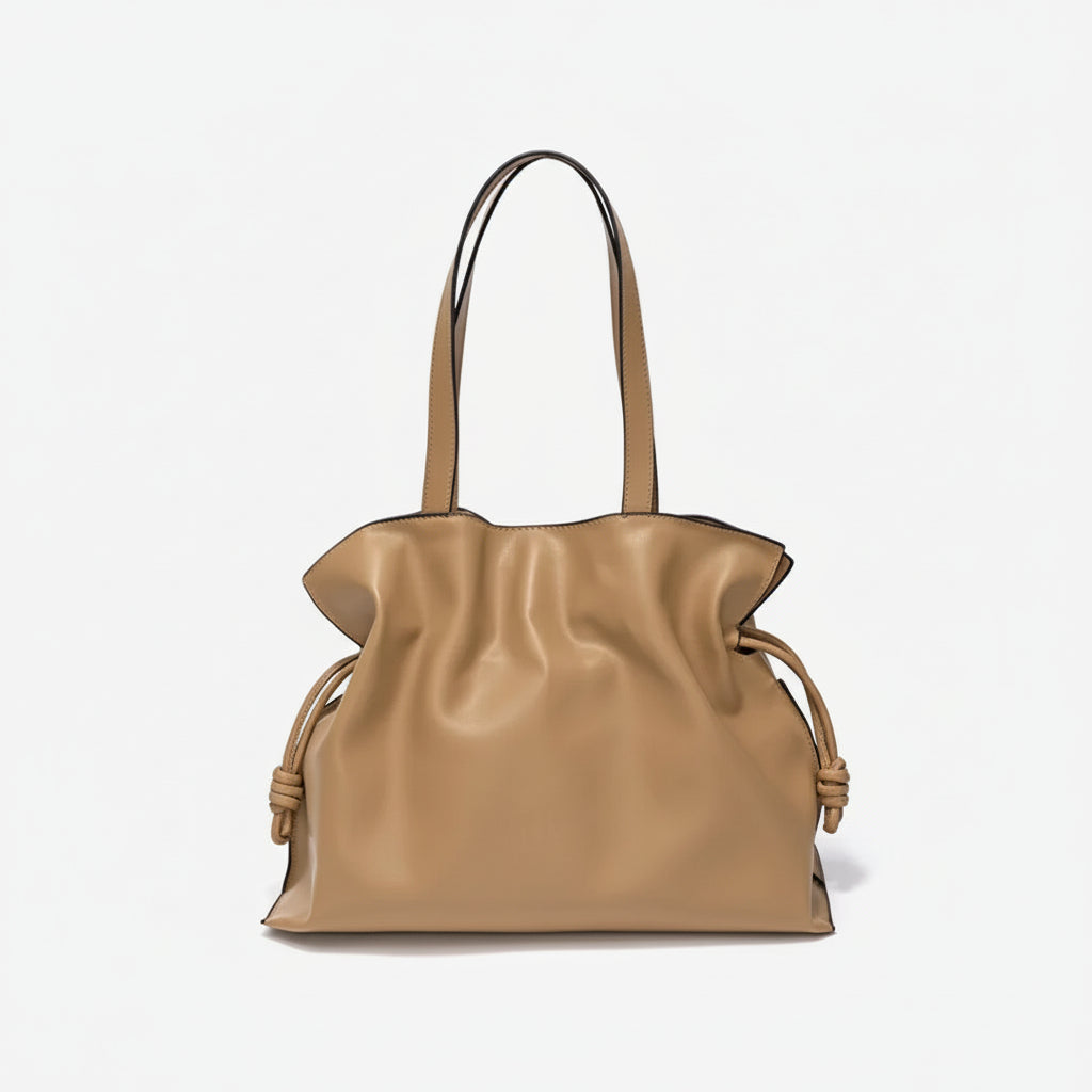 Beige leather tote bag with knotted side details and double handles on a white background