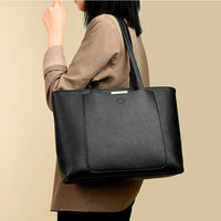 Woman in tan blazer carrying large black leather tote bag over shoulder