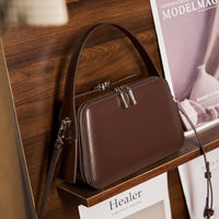 Brown leather handbag with silver zippers on wooden shelf with magazines