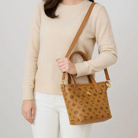Woman in beige sweater holding brown patterned leather crossbody handbag
