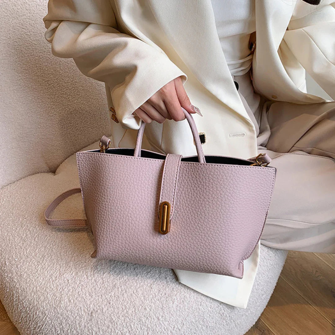 Woman in cream suit holding a textured light pink leather handbag on a beige chair