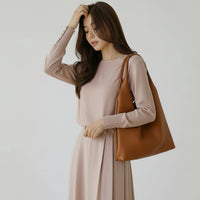 Woman in beige dress holding large brown leather tote bag on neutral background