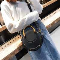 Woman wearing white sweater and denim skirt with round black crossbody purse, gold studs