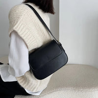 Woman wearing cream knit vest and white shirt with black leather crossbody bag