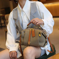 Woman in white blouse with gray vest holding a stylish taupe leather handbag with brown straps