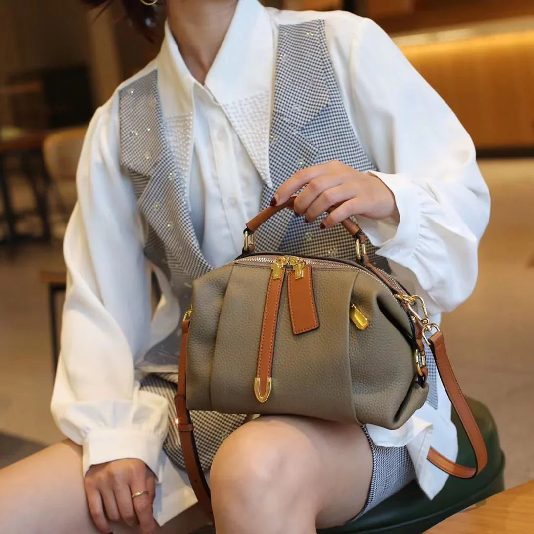 Woman in white blouse with gray vest holding a stylish taupe leather handbag with brown straps