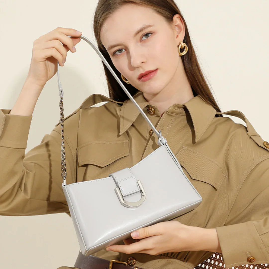 Woman in beige shirt dress holding a shiny gray shoulder bag with chain strap