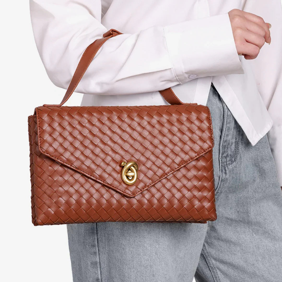 Brown woven leather handbag with gold clasp, held by woman in white shirt and jeans