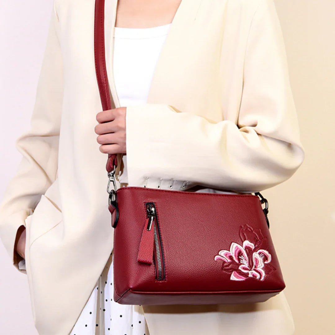 Woman in cream blazer with red leather crossbody bag, floral embroidery, and zipper pocket
