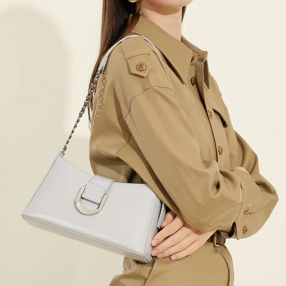 Woman in tan shirt dress holding a gray leather shoulder bag with chain strap