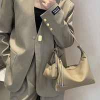 Woman in beige suit holding a tan leather shoulder bag against a neutral wall