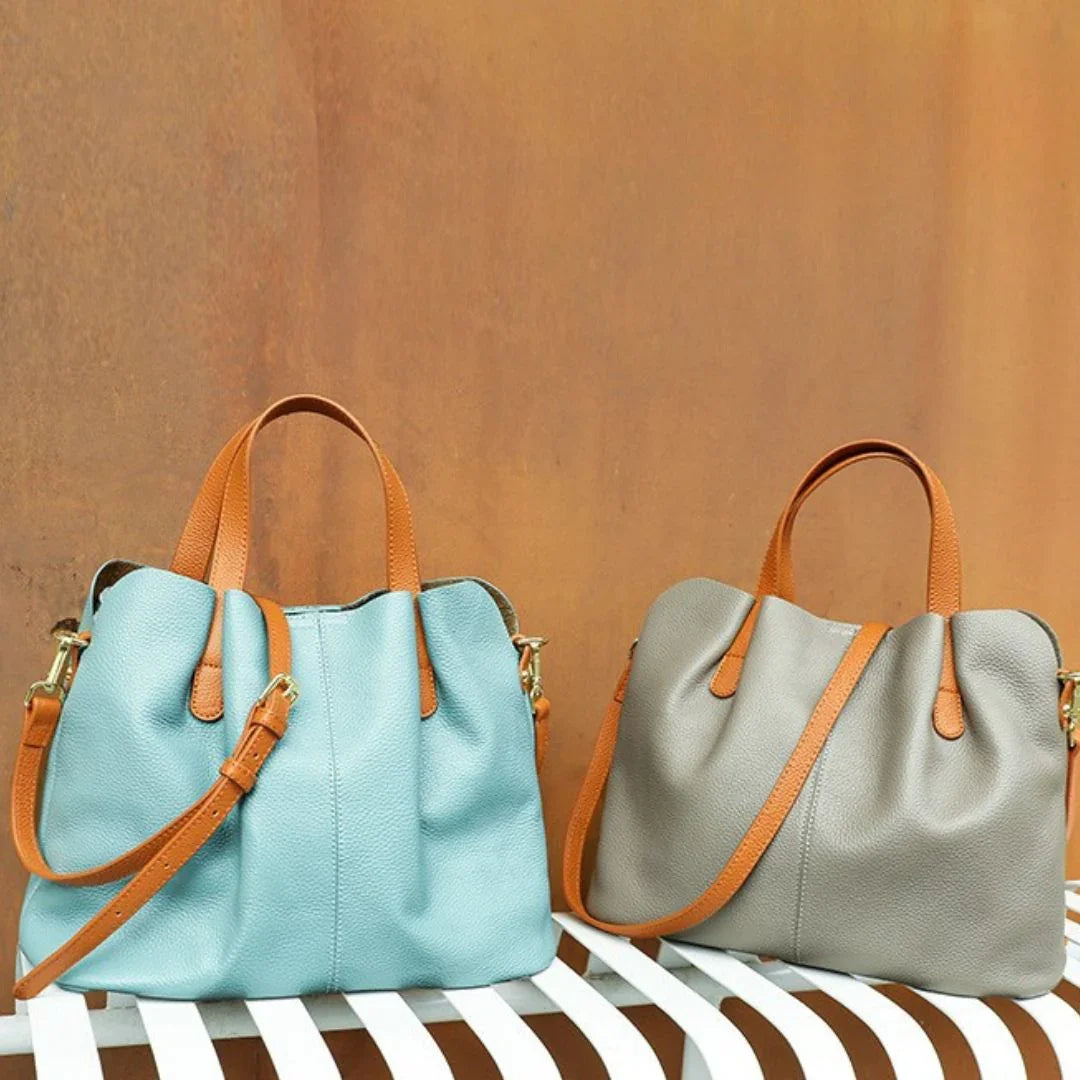 Blue and grey leather handbags with tan straps on a white bench, brown wall background