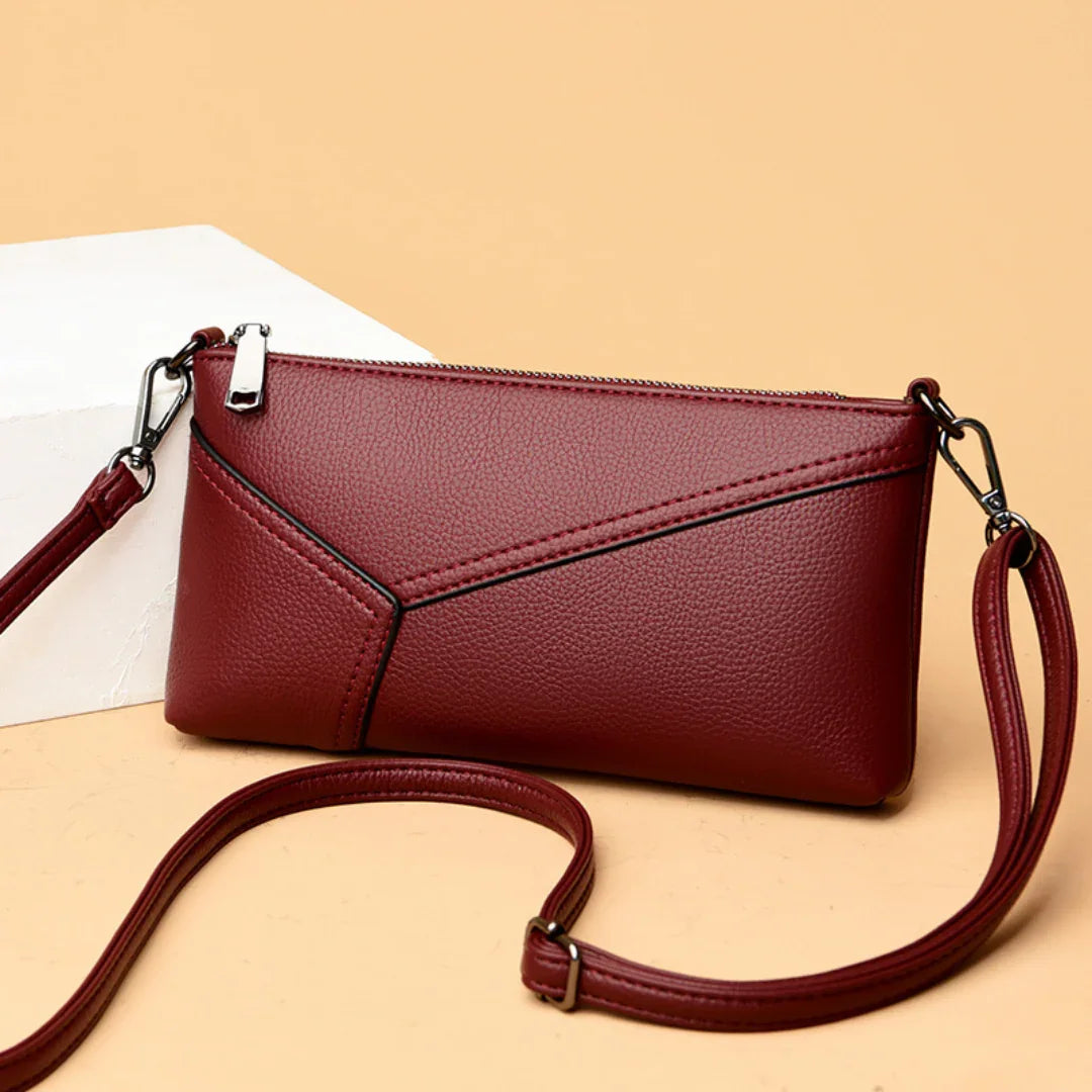 Burgundy leather crossbody purse with geometric stitching on beige background