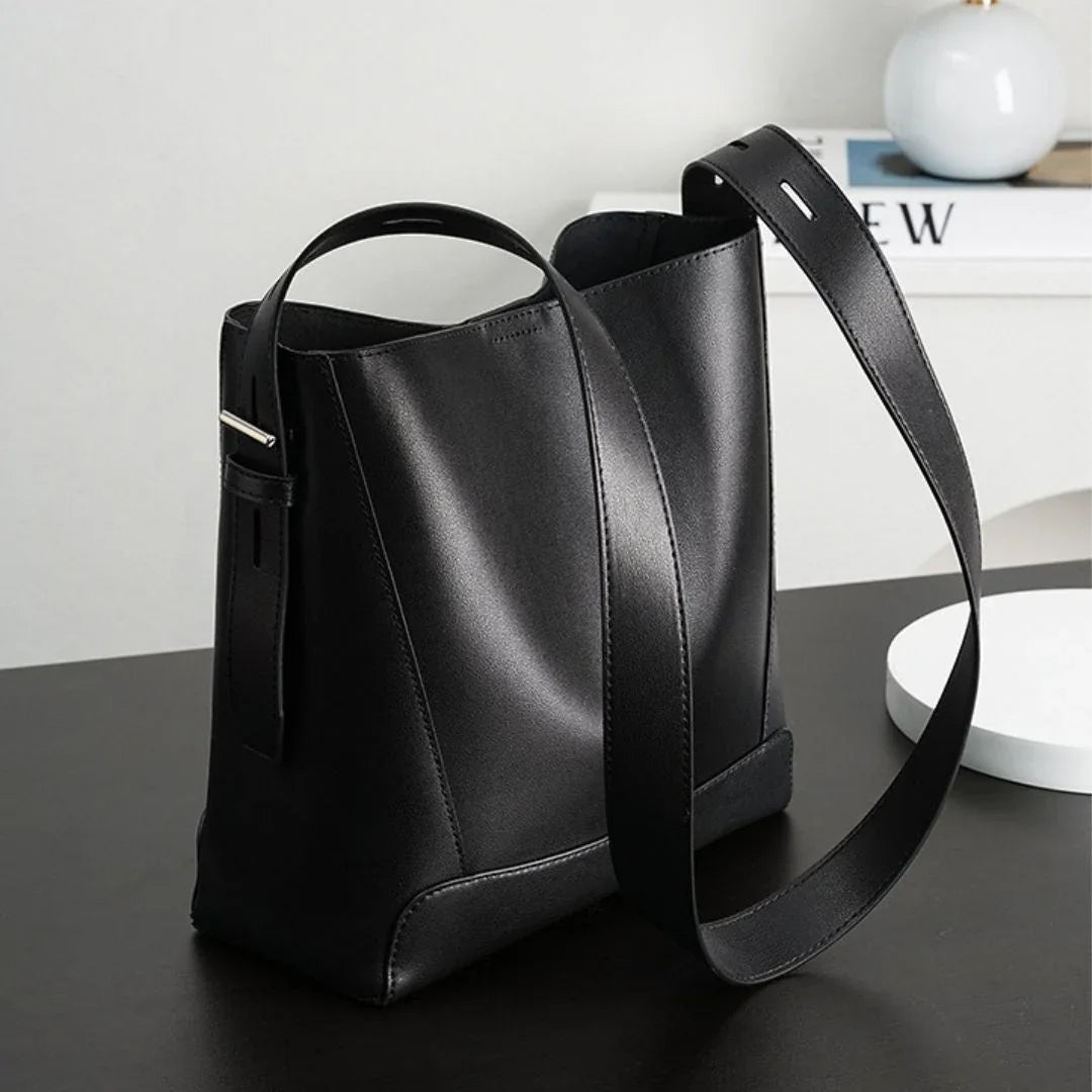 Minimalist black leather shoulder bag on a modern black desk with decor