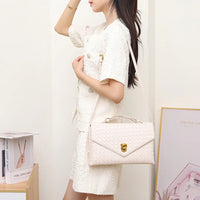 Woman in cream tweed outfit holding a woven cream shoulder bag, minimalist interior