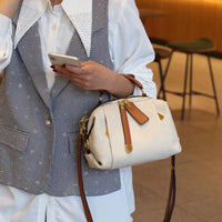 Woman in checkered vest holding cream leather crossbody bag with brown straps in cafe