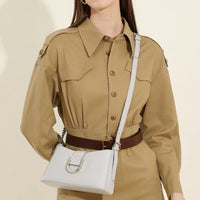 Woman in tan shirt dress with brown belt and white crossbody leather handbag