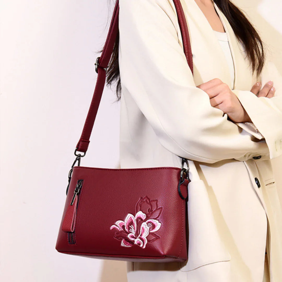 Burgundy shoulder bag with floral embroidery and zipper, worn over a cream blazer