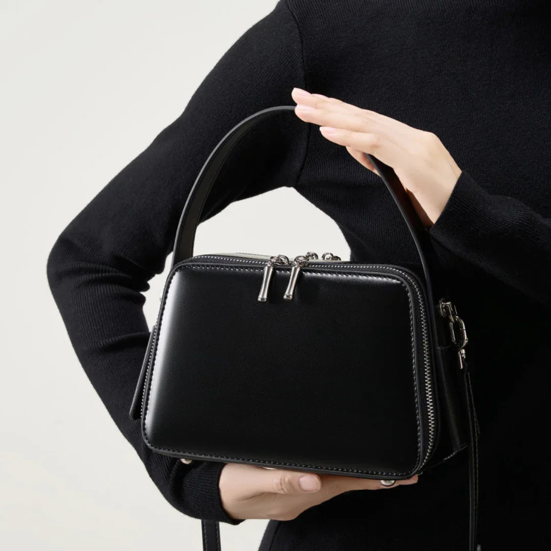 Woman holding a black leather handbag with silver hardware and zip closure