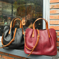 Black and burgundy leather tote handbags with brown straps displayed on a windowsill