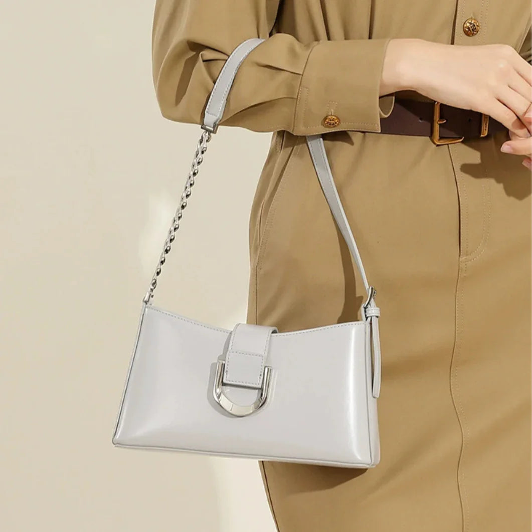 Woman in beige dress holding white leather shoulder bag with silver buckle
