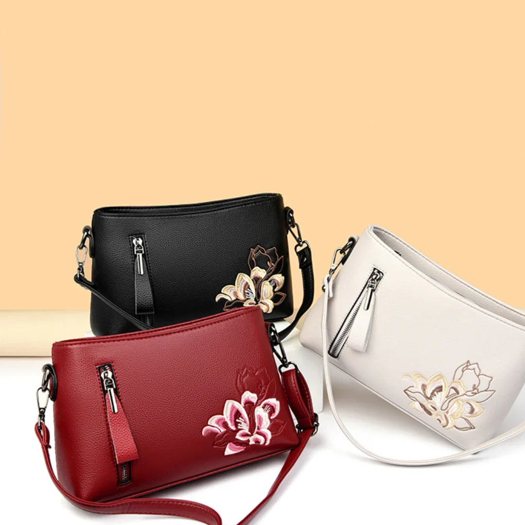 Three floral embroidered crossbody handbags in black, red, and white on a beige background