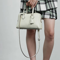 Woman in plaid outfit holding a stylish white leather handbag with strap