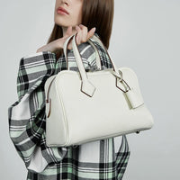 Woman in plaid coat holding a white leather handbag with top handles
